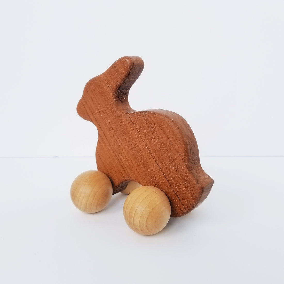 Dark wood rabbit toy with ball wheels on a white background